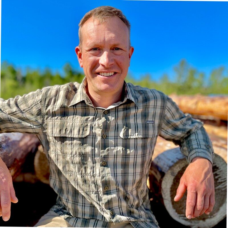 Nathan Demers in front of a log foundation.